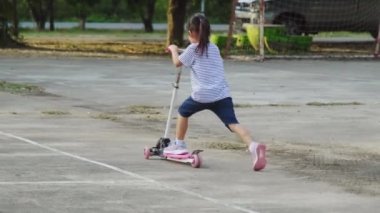 Yaz günü parkta motosikletle gezen sevimli küçük kızlar. Scooter 'la dışarıda oynayan bir kız. Çocuk için aktif eğlence ve açık hava sporu