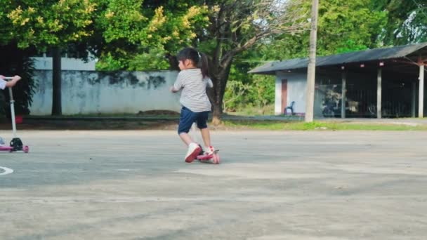 夏の日に屋外公園の路上でスクーターに乗る2人のかわいい女の子 子供たちはスクーターで屋外で遊ぶ 子供のためのアクティブなレジャーや屋外スポーツ — ストック動画