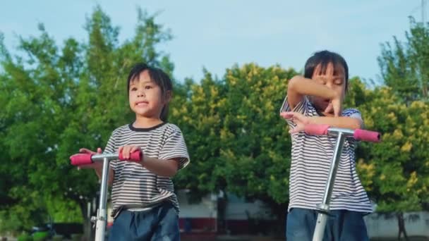 夏の日に屋外公園の路上でスクーターに乗る2人のかわいい女の子 子供たちはスクーターで屋外で遊ぶ 子供のためのアクティブなレジャーや屋外スポーツ — ストック動画