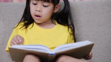 Evdeki kanepede oturmuş kitap okuyan tatlı küçük kız..