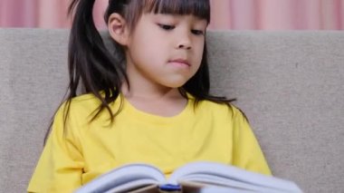 Evdeki kanepede oturmuş kitap okuyan tatlı küçük kız..