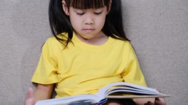 Evdeki kanepede oturmuş kitap okuyan tatlı küçük kız..