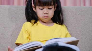 Evdeki kanepede oturmuş kitap okuyan tatlı küçük kız..