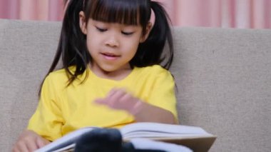 Evdeki kanepede oturmuş kitap okuyan tatlı küçük kız..