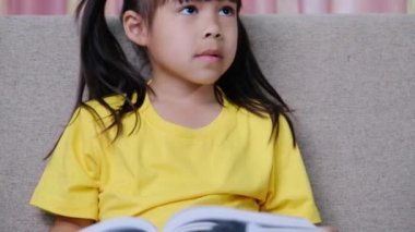 Evdeki kanepede oturmuş kitap okuyan tatlı küçük kız..