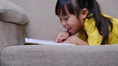 Evdeki kanepede oturmuş kitap okuyan tatlı küçük kız..