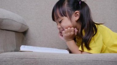 Evdeki kanepede oturmuş kitap okuyan tatlı küçük kız..