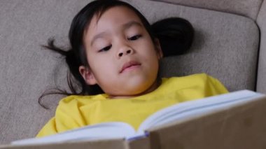 Evdeki kanepede oturmuş kitap okuyan tatlı küçük kız..