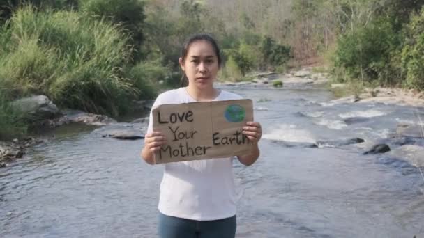 森の滝であなたの母なる地球のポスターを愛する女性の肖像画 女性ボランティア活動家は環境を守ることを示す 世界環境デー — ストック動画