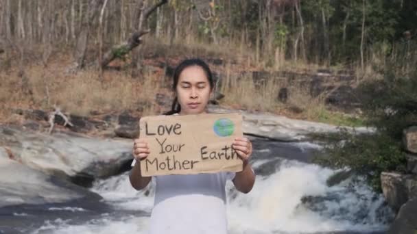 站在森林瀑布边的 爱你的地球母亲 海报上的女性画像 女志愿人员活动者展示了保护环境的情况 世界环境日 — 图库视频影像