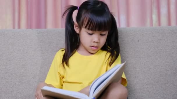 Sød Lille Pige Læser Bog Mens Sidder Sofaen Derhjemme – Stock-video