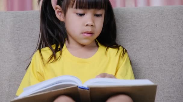 Cute Little Girl Reading Book While Sitting Sofa Home — Stock Video