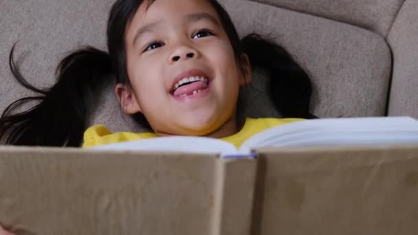 Cute Little Girl Reading Book While Sitting Sofa Home — Stock Video