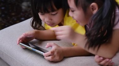 İki kız kardeş evdeki kanepede oturmuş akıllı telefonlarıyla oyun oynuyorlar. Modern iletişim ve alet bağımlılığı kavramı. Elinde aletler olan iki çocuk..