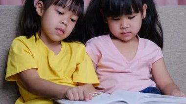 Evdeki kanepede uzanmış kitap okuyan sevimli Asyalı kız kardeşler..