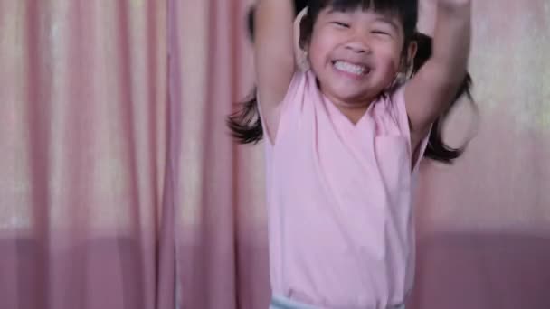 一个穿着粉色衣服的可爱小女孩快乐地在家里跳跃的画像 活跃的女孩感到自由 面部表情和手势的概念 — 图库视频影像