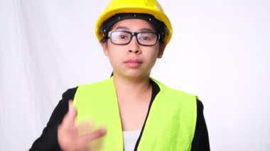 Kadın teknisyen kaskla gülümsüyor ve baş parmağını kaldırıyor. Stüdyoda beyaz arka planda kendine güvenen bir inşaat işçisi..