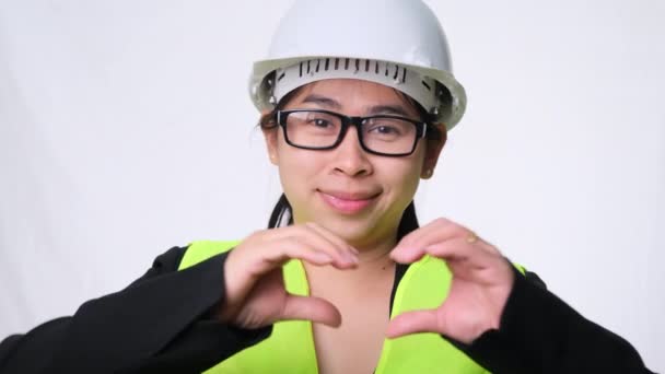 ヘルメットと笑顔ヘルメットで女性エンジニアと心臓の形を見せます手で白い背景にスタジオ — ストック動画