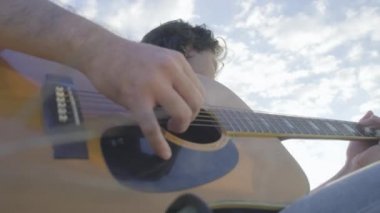 Yakışıklı kıvırcık saçlı Asyalı adam gün batımında göl kenarında gitar çalıp şarkı söylüyor..