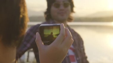 Yakışıklı kıvırcık saçlı Asyalı adam gün batımında göl kenarında gitar çalıp şarkı söylüyor..