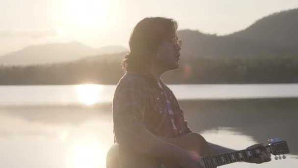 Guapo Rizado Asiático Hombre Tocando Guitarra Cantando Junto Lago Atardecer — Vídeo de stock