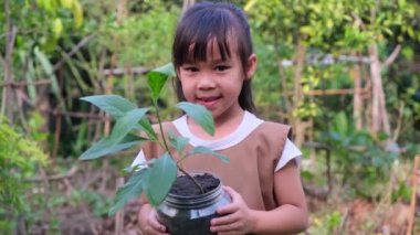 Baharda bulanık yeşil bir arka planda, geri dönüşüm kabında küçük bir ağaç tutan sevimli küçük bir kız. Dünya günü ekoloji kavramı
