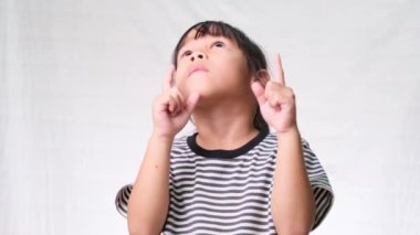 Küçük şirin kız boş bir yere bakıyor ve işaret ediyor. İki eli de beyaz stüdyonun arka planında..