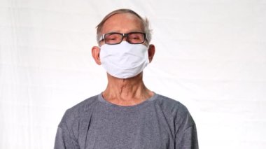 Beyaz arka planda tıbbi maske takan son sınıf öğrencisi. Covid-19 önleme kampanyası için maske takan yaşlı bir adam