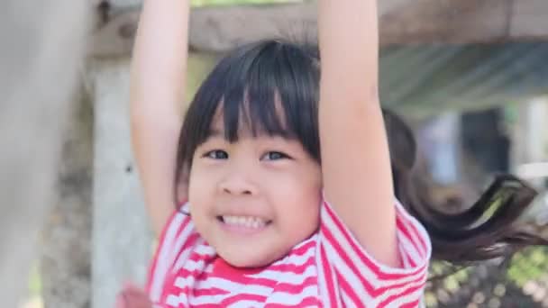 可爱的亚洲小女孩用双手挂着一个木制的酒吧 在后院操场上锻炼 活力充沛的孩子用双手吊在吧台上 — 图库视频影像