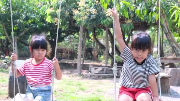 两个可爱的亚洲姐妹坐在夏日花园的秋千上吵架 困难的家庭关系 — 图库视频影像
