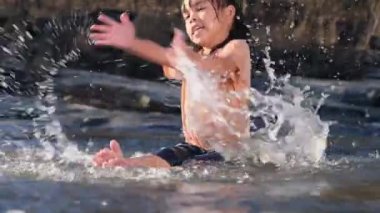 Orman deresinde kız kardeşiyle oynayan Asyalı küçük kız. Yazın nehirde çocuklarla aktif eğlence..