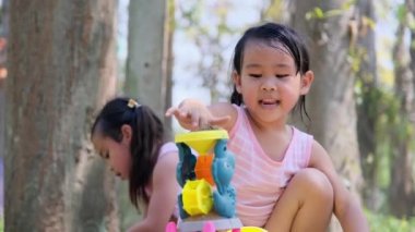 İki küçük kız kardeş kumların arasında plastik oyuncaklarla dışarıda oynayarak eğleniyorlar..