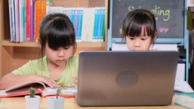 İki Asyalı kız öğrenci evde bilgisayarla Zoom 'u arıyor. İki küçük kız karantina sırasında evde öğreniyor. Yeni Normal. Evde eğitim.