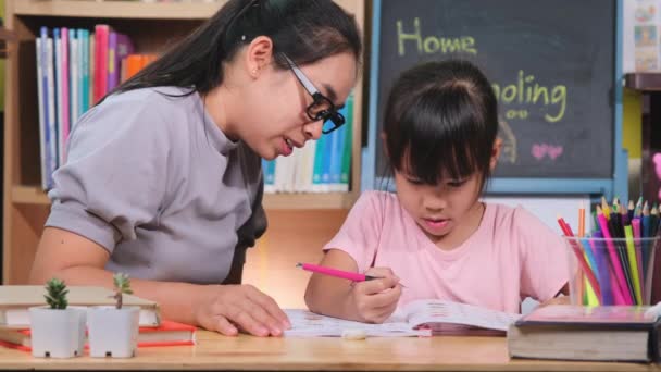 アジア系の少女は母親と隔離中に家で勉強する 母は家で娘の宿題を手伝っている 家庭教育 — ストック動画