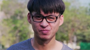 Gözlüklü, gri tişörtlü ve yaz bahçesinde duran kendinden emin bir gencin portresi..