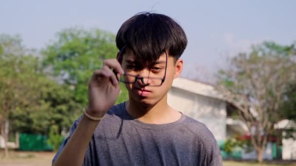 厌倦了的年轻亚洲人 在公园里用眼镜擦拭眼睛 — 图库视频影像
