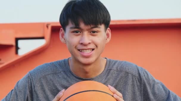 Genç Basketbolcu Sahanın Kenarında Oturmuş Elinde Bir Topla Kameraya Gülümsüyor — Stok video