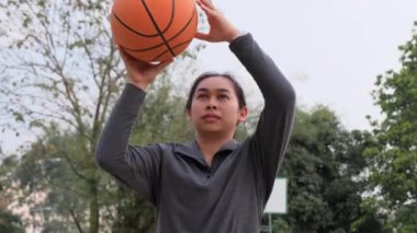 Spor giyimli Asyalı bir kadın dışarıda basketbol oynuyor. Bayan basketbolcular yerel kortlarda antrenman yapıyor..