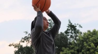 Kulaklık takan Asyalı bayan sporcu basketbol sahasında basketbol pozu veriyor.