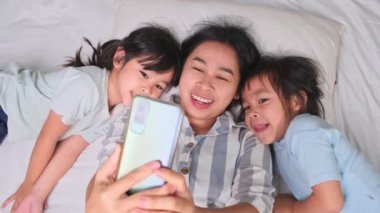 Mutlu Asyalı aile rahat evlerinde akıllı telefonlarıyla eğleniyor. Gülümseyen anne ve güzel kızlar telefon kullanıyor, evde hatırlamak için selfie ya da video çekiyorlar. Evde iyi vakit geçir.
