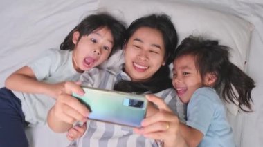 Mutlu Asyalı aile rahat evlerinde akıllı telefonlarıyla eğleniyor. Gülümseyen anne ve güzel kızlar telefon kullanıyor, evde hatırlamak için selfie ya da video çekiyorlar. Evde iyi vakit geçir.