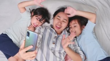 Mutlu Asyalı aile rahat evlerinde akıllı telefonlarıyla eğleniyor. Gülümseyen anne ve güzel kızlar telefon kullanıyor, evde hatırlamak için selfie ya da video çekiyorlar. Evde iyi vakit geçir.