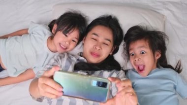 Mutlu Asyalı aile rahat evlerinde akıllı telefonlarıyla eğleniyor. Gülümseyen anne ve güzel kızlar telefon kullanıyor, evde hatırlamak için selfie ya da video çekiyorlar. Evde iyi vakit geçir.