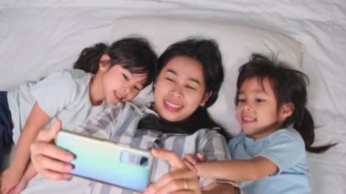 Mutlu Asyalı aile rahat evlerinde akıllı telefonlarıyla eğleniyor. Gülümseyen anne ve güzel kızlar telefon kullanıyor, evde hatırlamak için selfie ya da video çekiyorlar. Evde iyi vakit geçir.