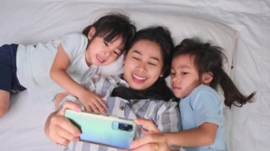 Mutlu Asyalı aile rahat evlerinde akıllı telefonlarıyla eğleniyor. Gülümseyen anne ve güzel kızlar telefon kullanıyor, evde hatırlamak için selfie ya da video çekiyorlar. Evde iyi vakit geçir.