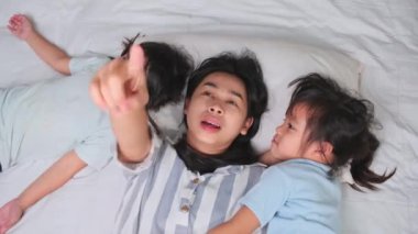 Mutlu çocukların evdeki bir yatakta anneleriyle oynayıp kameraya baktıklarının en üst görüntüsü. Evde iyi vakit geçir..