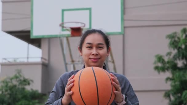 アジアの女性は屋外バスケットボールの遊び場でカメラを見てバスケットボールを保持 — ストック動画