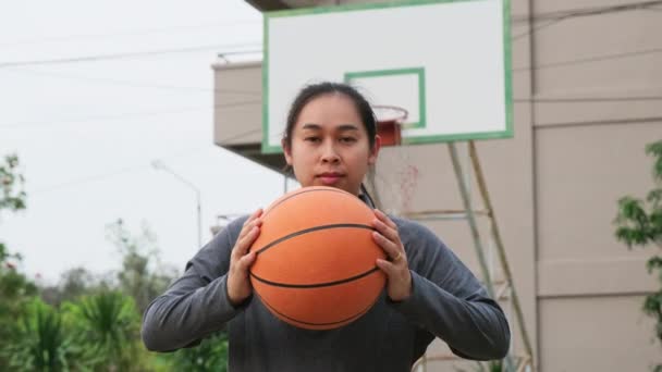 Азиатка Держащая Баскетбол Смотрит Камеру Открытой Баскетбольной Площадке — стоковое видео