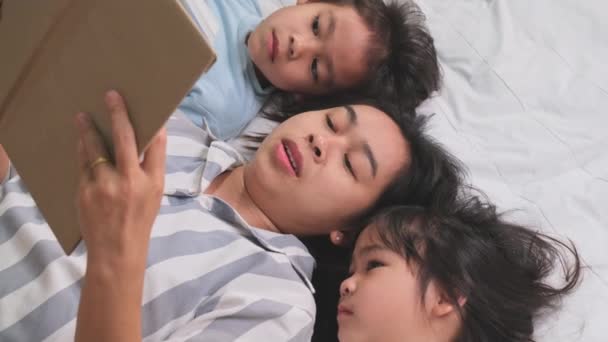 可爱快乐的亚洲家庭在舒适的家 漂亮的年轻母亲在家里的床上给女儿们读书 在家里玩的开心 — 图库视频影像