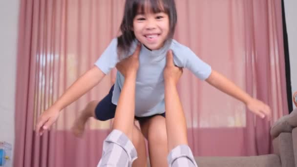 幸せな子供たちは家でお母さんと遊んでいる 母は暖かい床に横になり 彼女の小さな娘を持ち上げ 空を飛ぶことを楽しむ飛行機として自分自身を想像しています — ストック動画
